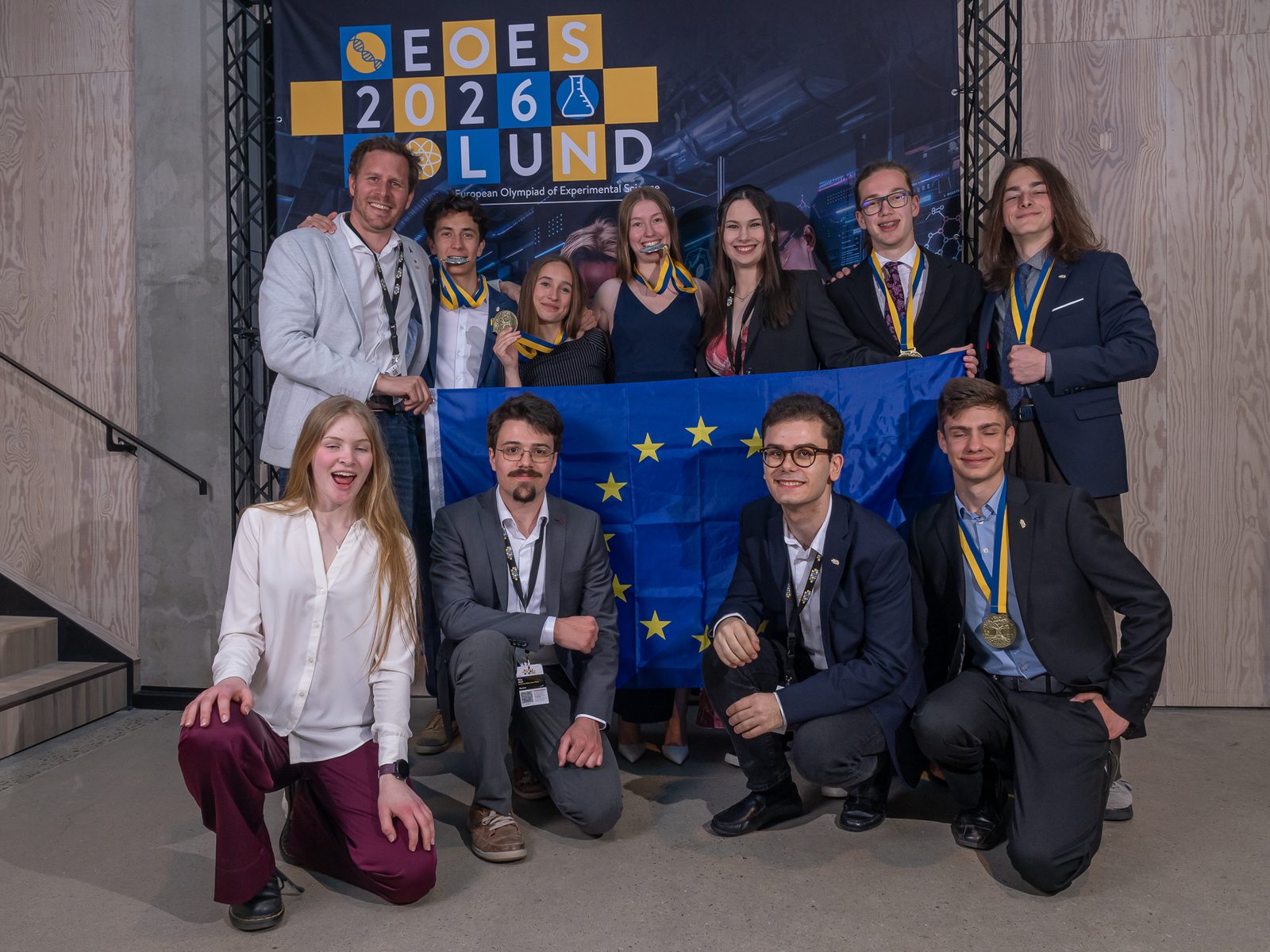 Die österreichische Delegation der EOES 2026 mit Medaillen und Europafahne vor dem Banner der EOES 2026 in Lund.